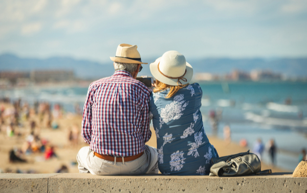 An older couple sitting on a wall at a beach.