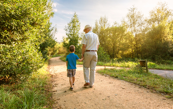 A grandfather and grandchild walking through a park.