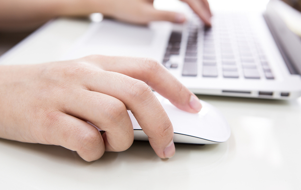 A person typing on a laptop keyboard and using a mouse.