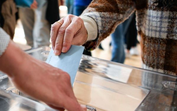 A person putting a ballot paper into a box.