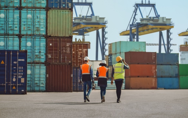 Workers walking through a shipping cargo container terminal depot.