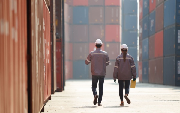 Two workers walking between shopping containers.