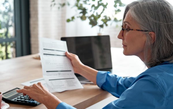 An older woman looking at a document and a calculator.